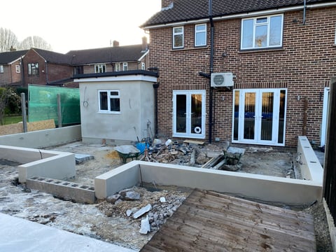 Home under renovation with concrete foundations, construction materials, and white build-out walls visible on brick house exterior