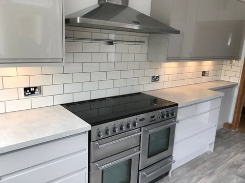 Modern white kitchen with stainless steel range cooker, black countertops, white subway tile backsplash, and chrome extractor hood