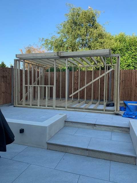 Metal frame pergola structure under construction in backyard with paved patio and white storage box
