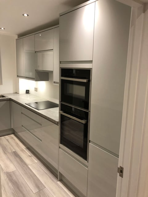 Modern kitchen with white cabinetry, built-in double ovens, black countertop, and stainless steel appliances