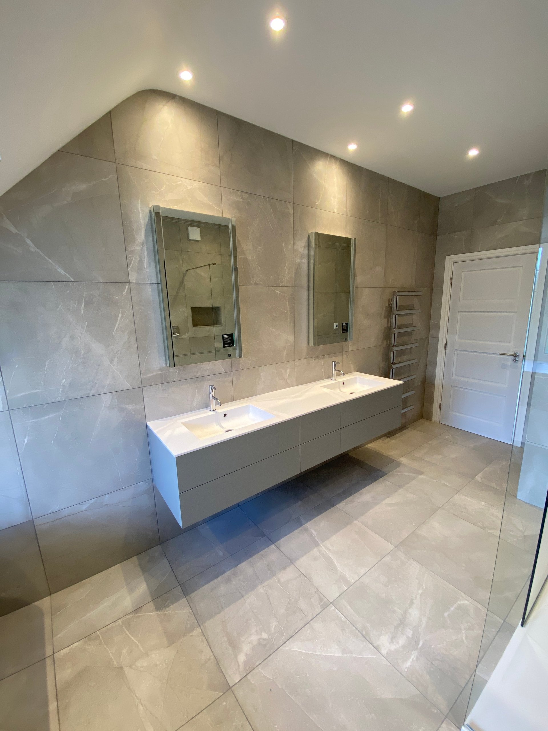 Modern bathroom with double vanity sink, large mirrors, tile flooring, glass shower enclosure, and recessed lighting