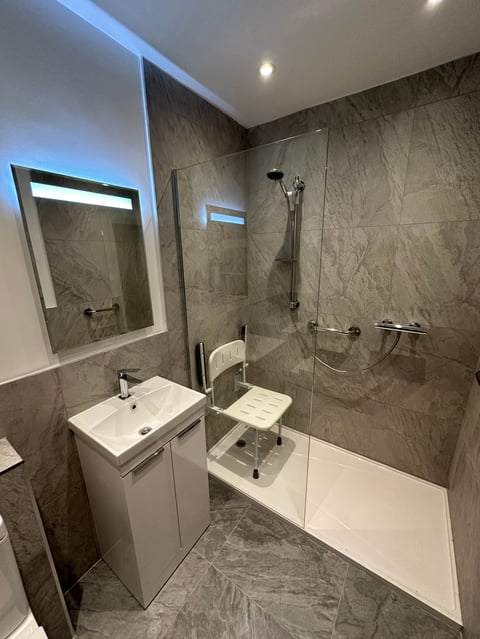 Modern bathroom with gray marble tile, white vanity with sink, illuminated mirror, and walk-in shower with glass enclosure