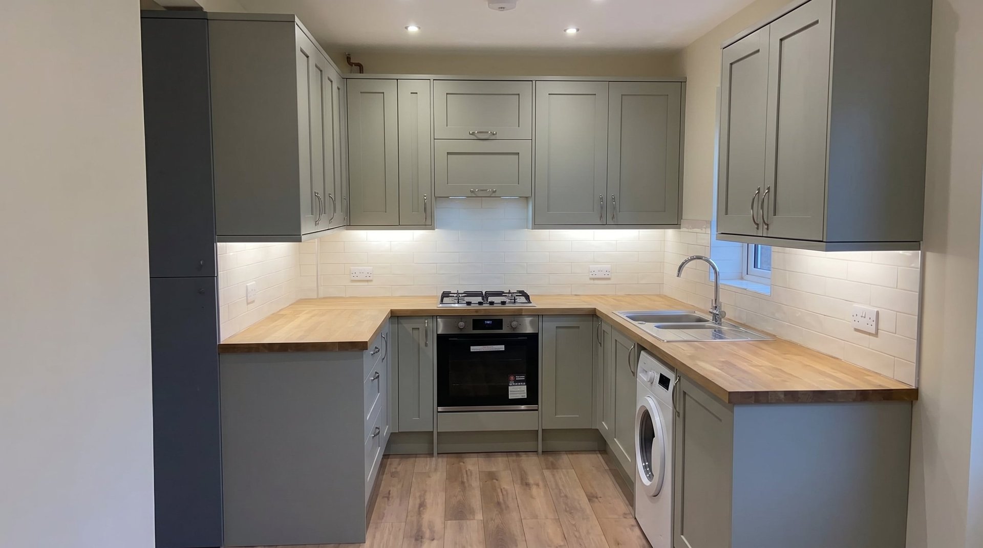 Modern kitchen with gray cabinetry, wooden countertops, gas range, and washing machine in compact u-shaped layout