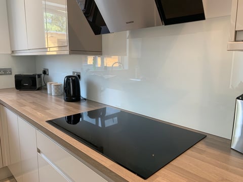Modern white kitchen with black induction cooktop, wood countertops, white backsplash, stainless steel appliances, and natural light from window