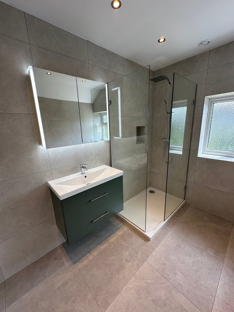 Modern bathroom with tiled walls, illuminated mirror, green vanity sink, and glass walk-in shower enclosure