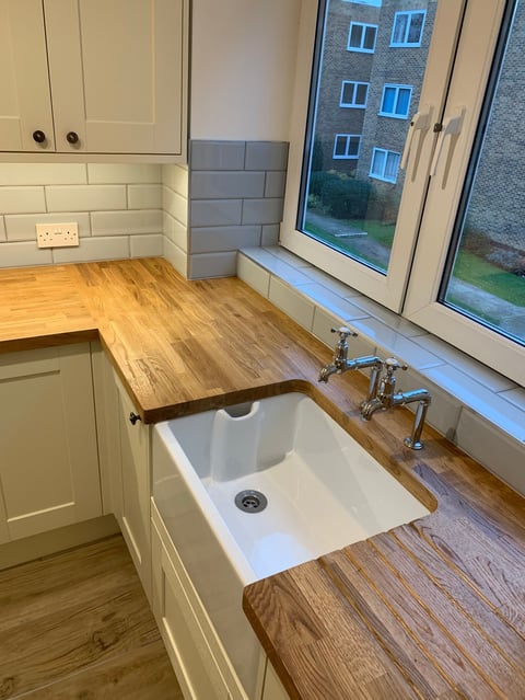 Modern kitchen with white undermount sink, chrome faucet, wooden countertops, cream cabinets, white subway tile backsplash, and large window overlooking residential building