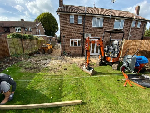 Backyard with orange mini excavator and construction equipment in front of brick house during landscaping work