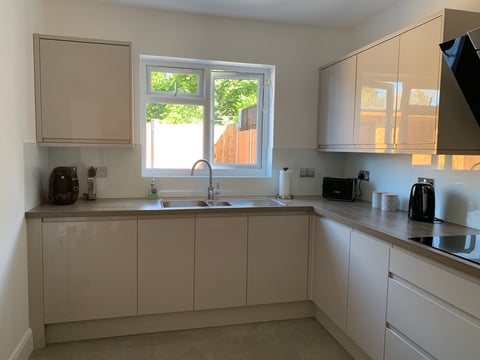 Modern beige kitchen with L-shaped counter, sink under window, stainless steel appliances, and cabinets with glass doors