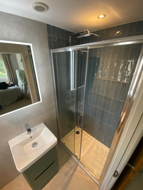 Modern bathroom with glass shower enclosure, wall-mounted sink, illuminated mirror, and dark tiled shower walls
