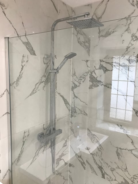 Modern bathroom shower enclosure with chrome fixtures and rainfall showerhead, surrounded by marble-pattern tile walls