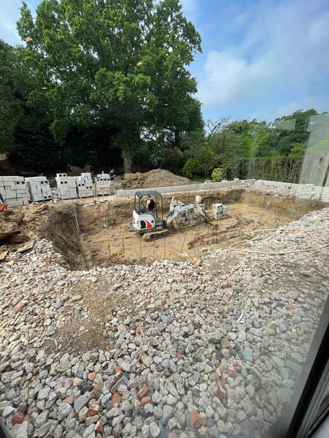 Construction site with mini excavator in gravel pit surrounded by trees and building materials on pallets