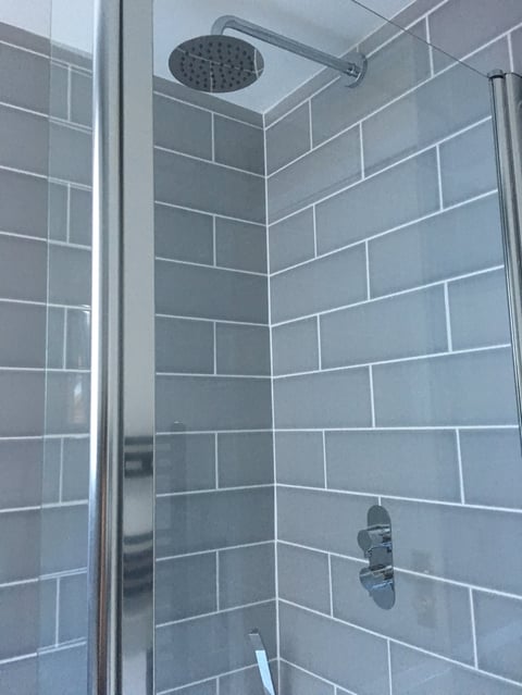 Modern shower enclosure with gray subway tile walls, chrome fixtures, overhead rainfall showerhead, and glass door