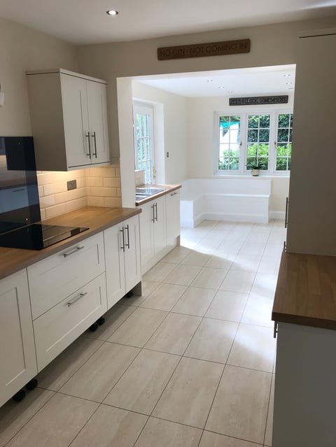 Modern kitchen with white cabinetry, wood countertops, and neutral tile flooring opening to a bright dining area with large windows