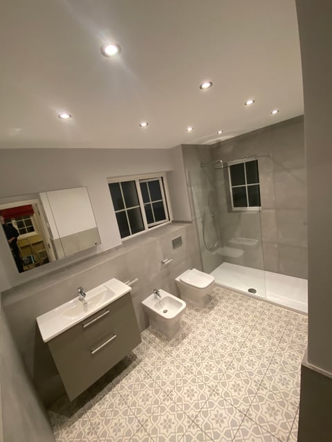 Modern bathroom interior with white vanity, toilet, walk-in shower, patterned tile floor, and recessed ceiling lights