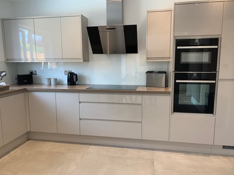 Modern white kitchen with glossy cabinetry, stainless steel appliances, and minimalist design with light wood flooring