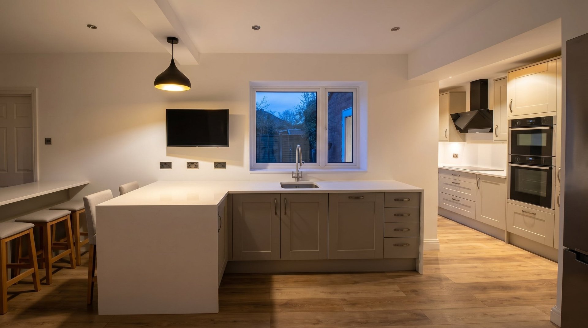 Modern kitchen with white and gray cabinetry, island counter, stainless steel appliances, and blue-tinted windows at dusk