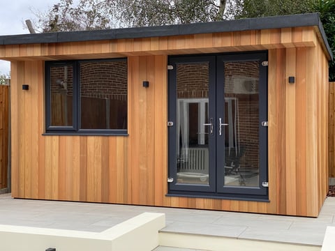 Modern wooden garden studio with black-framed windows and double doors on a concrete foundation