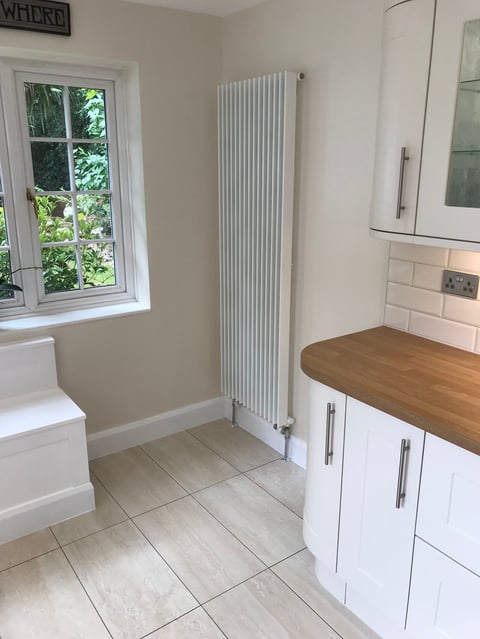 Modern bathroom with white cabinetry, wooden countertop, tall radiator, tiled floor, and window overlooking greenery
