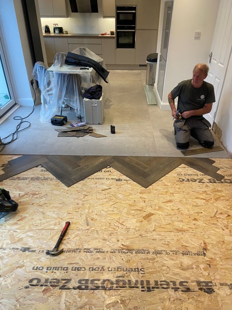 Worker installing flooring in a kitchen renovation, with protective coverings and herringbone pattern tiles visible on subfloor